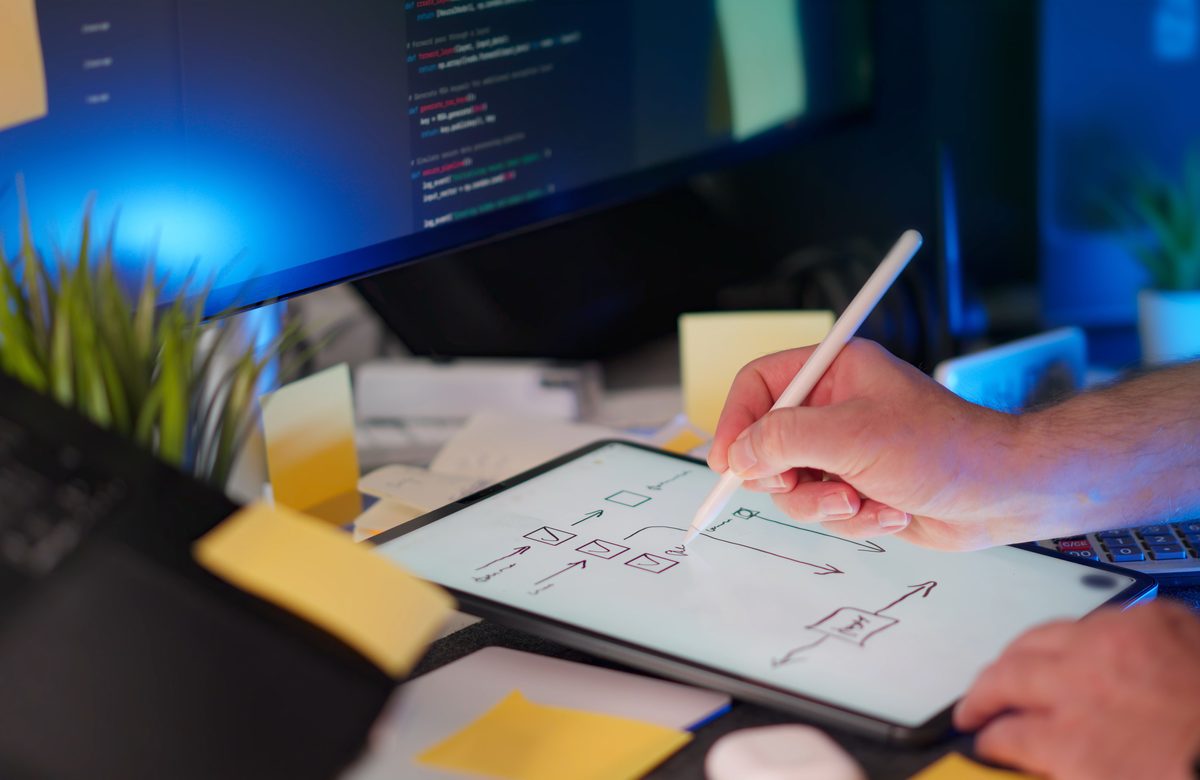 Maquette d'interface dessinée sur une tablette, à côté d'un écran de code